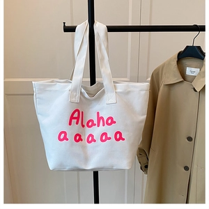 Close-up of white canvas tote bag with pink Alaha lettering and dual shoulder straps
