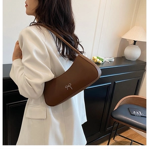 Detail of a brown leather hobo bag with a silver bow accent shown in a cozy indoor setting