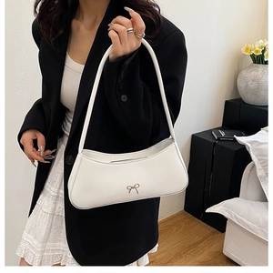 Close-up of white leather baguette bag featuring a silver bow accent and slim shoulder strap