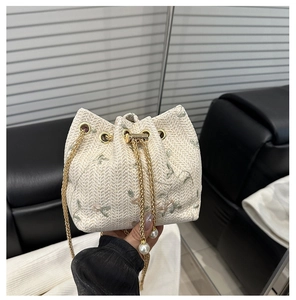 Close-up of woven cream bucket bag with floral embroidery and gold chain pearl strap
