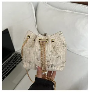 Close-up of lace straw bucket bag with floral embroidery, pearl drawstring and gold chain