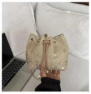 Detail of woven bucket bag with floral embroidery, chain drawstring and pearl accents