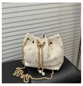Detail of floral embroidery and gold chain on beige straw bucket bag with pearl drawstring