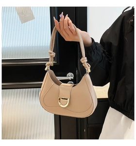 Détail du sac demi-lune en cuir beige avec boucle dorée en D et anse à nœud élégante