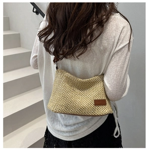 Détail d'un sac en paille tressée beige avec un écusson en cuir brun et bandoulière