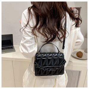 Detail view of black quilted crossbody bag with chain and handle on a model