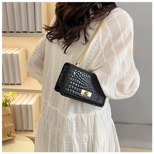 Detail of black stone-patterned crossbody bag with gold chain strap on a model