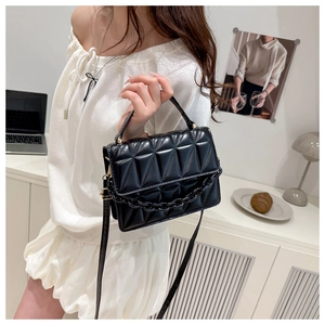 Detail view of a black quilted crossbody bag with a thick resin chain and top handle strap