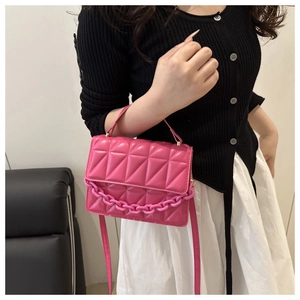 Detail of rose red quilted crossbody bag featuring bold plastic chain and geometric pattern