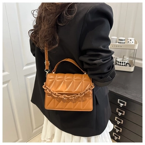 Close-up of caramel quilted crossbody bag with decorative chain on a model
