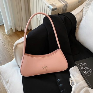 Pink minimalist faux leather shoulder bag with gold bow clasp on a white sofa decor