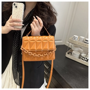 Detail of orange quilted crossbody bag with chunky chain and geometric stitching