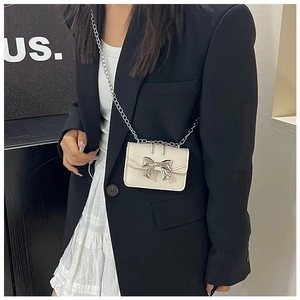 Close-up of white mini crossbody bag featuring a silver metal bow and chain strap