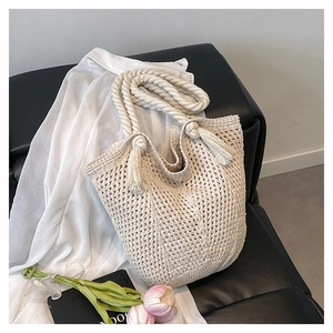 Detail of hand-woven cream tote bag with rope handle, tassel charm, and cotton texture