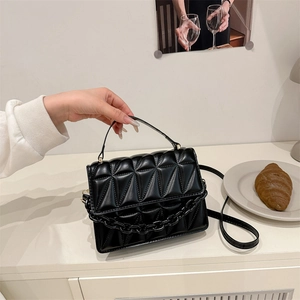 Quilted black flap handbag with chunky chain decor and gold hardware on white surface