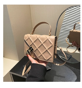 Detail of apricot quilted crossbody bag with metal lock and chain strap on a desk