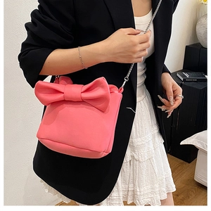 Detailed view of peach pink bow bucket bag with silver chain strap on black blazer