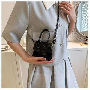 Detail of a mini black crocodile pattern crossbody bag held by a model for scale