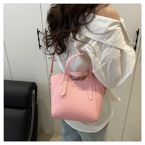Rear view of a model wearing the light pink lychee grain leather bucket bag with top handle