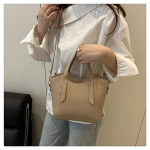Detail of elegant beige pebbled leather bucket bag carried by model in casual outfit