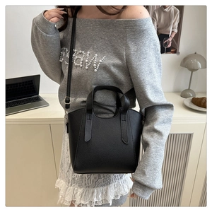 Detail of black lychee texture leather bucket bag with dual handles and thin strap