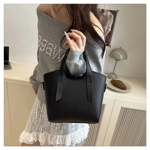 Detail of black litchi grain leather tote bag with elongated handles in a lifestyle setting