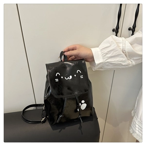 Detail of a small black faux leather backpack with a white cartoon cat face and paw prints