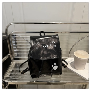 Detail of a black patent leather backpack featuring cute white cat face and paw prints