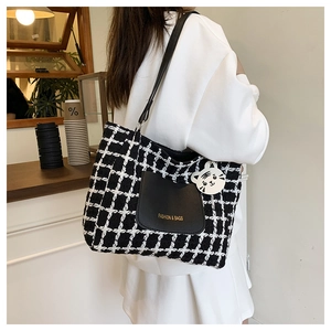 Detail of checkered woven tote bag with leather pocket and plush tiger charm on shoulder