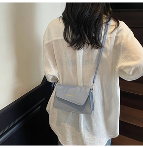 Close-up of light blue crossbody bag with gold fashion lettering and textured finish