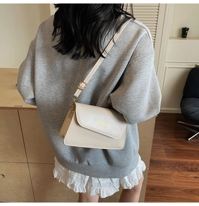 Detail of cream crossbody bag with textured weaving and gold hardware on model