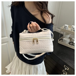 Detailed close-up of white woven texture and golden zipper on the square handbag