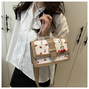 Detail of crossbody bag with cherry print, gold hardware, and 3D cherry charm accessory