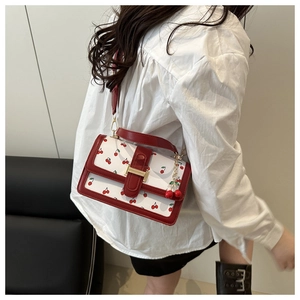 Close-up of white crossbody bag with red cherry print and gold clasp details