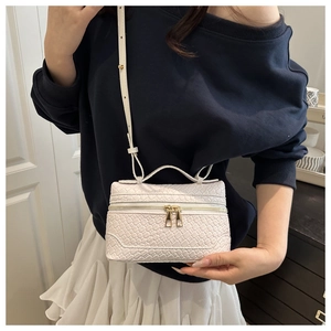 Close-up of white woven box bag featuring gold double zippers and elegant top handle