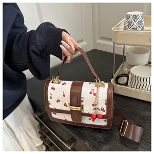 Detail of white handbag with cherry print, brown leather trim and cherry charm