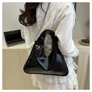 Close-up of a glossy black pleated dumpling bag with a delicate silver chain strap