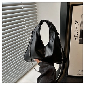 Detail of glossy black handbag with silver chain strap and twisted handle design