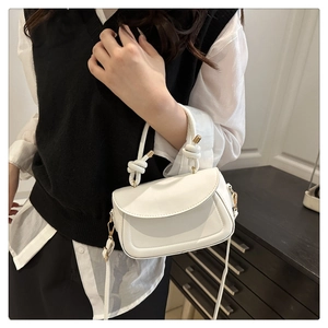 Detail of white mini crossbody bag featuring a decorative knot handle and gold hardware
