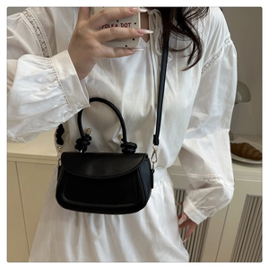 Detail of black leather crossbody bag with knot handle and metal buckle in lifestyle setting