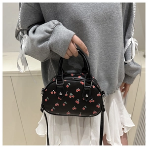 Detail of black cherry print handbag held by model showing compact size and PU leather texture