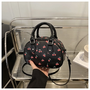 Detail of black faux leather handbag featuring cherry prints and adjustable shoulder strap
