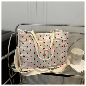 Detail of beige corduroy tote bag with red heart patterns and adjustable shoulder strap