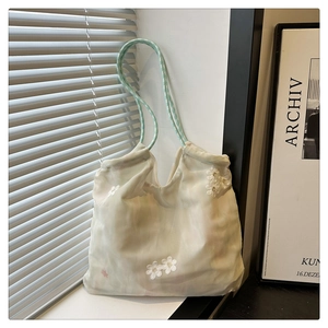 Detail of white mesh tote bag featuring delicate daisy embroidery and green checkered handles