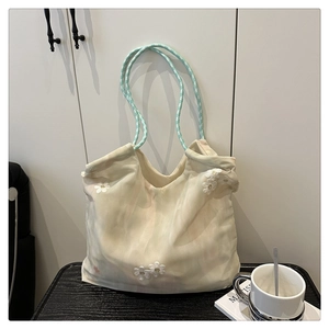 Detailed view of beige tote bag featuring white daisy embroidery and green checkered straps