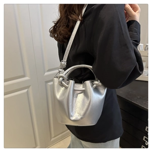 Detail of silver metallic bucket bag with drawstring folds and knotted handle on shoulder