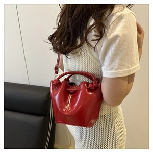 Detail of red glossy bucket bag featuring twisted handle and adjustable shoulder strap