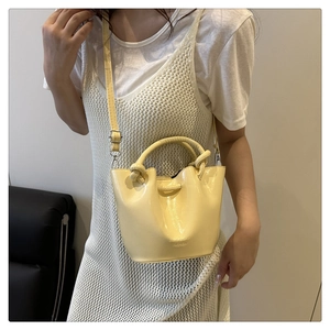 Detail showing pale yellow glossy bucket bag with embossed logo and elegant metal handle