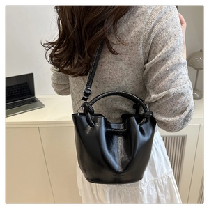 Detail of a chic black bucket bag with glossy finish and adjustable crossbody strap