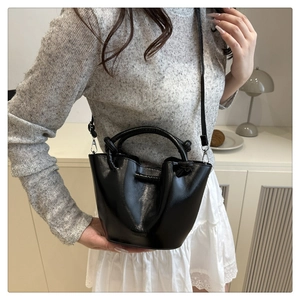 Detailed shot of black bucket bag featuring double handles and long strap with metallic buckles